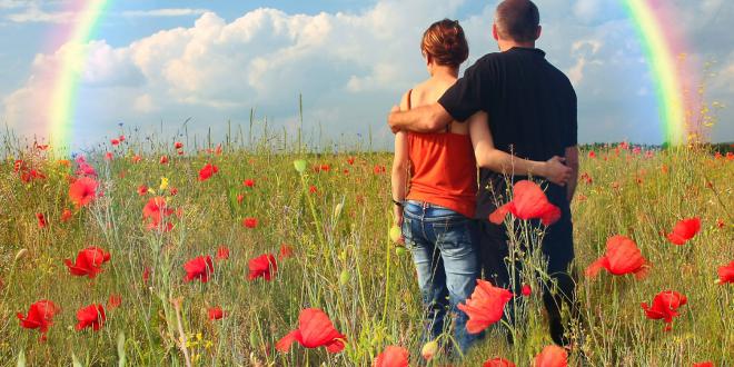 a couple in a field looking toward a rainbow